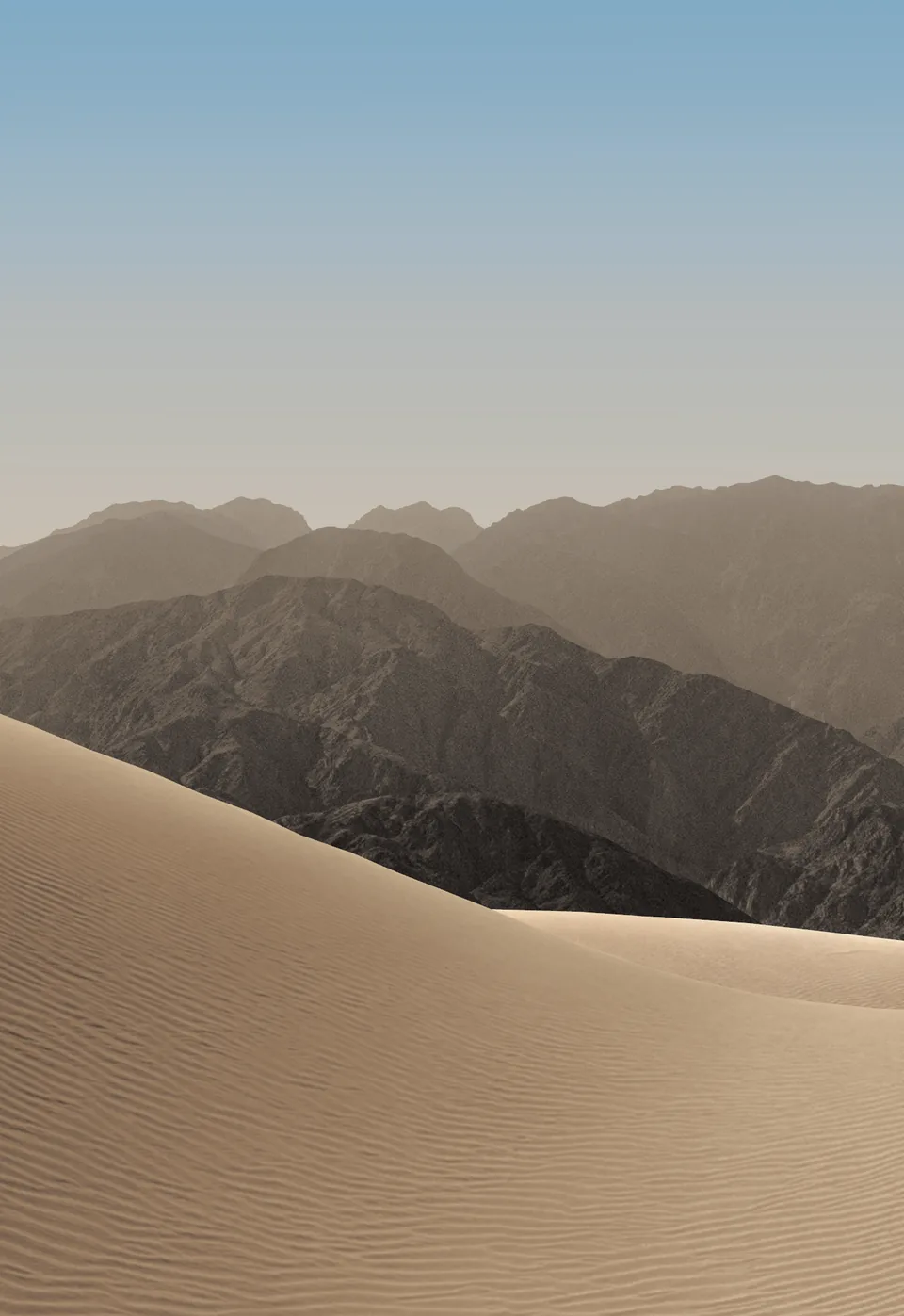 iPhone Duo default outer display Home Screen wallpaper, light version: pale sand dunes and hazy mountains under a soft blue morning sky.