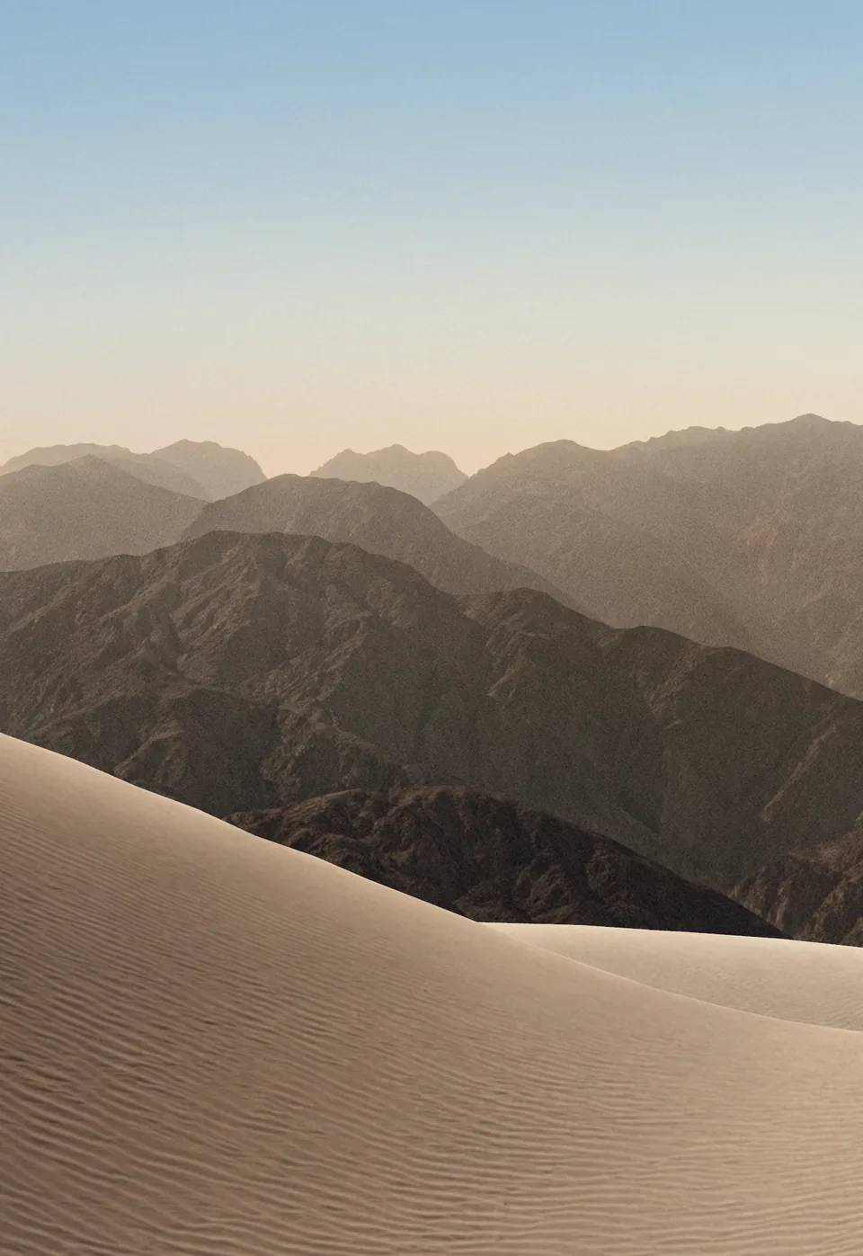 iPhone Duo default outer display Lock Screen wallpaper, light version: pale sand dunes and hazy mountains under a soft blue morning sky.
